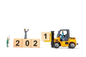 Miniature workers teaming up to create wooden blocks with the number 2021, Happy New Year concept photo