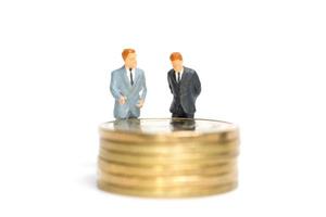 Empresarios en miniatura de pie sobre una pila de monedas, dinero y concepto financiero