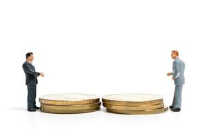 Empresarios en miniatura de pie sobre una pila de monedas, dinero y concepto financiero