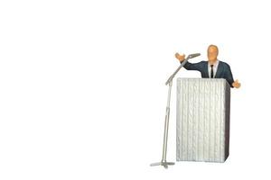Político en miniatura hablando con un micrófono aislado sobre un fondo blanco. foto