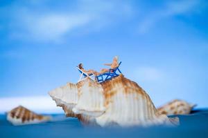 Gente en miniatura tomando el sol en una concha con un fondo de cielo azul, concepto de vacaciones de verano foto