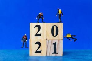 Miniature divers diving around wooden blocks with the number 2021, Happy New Year concept photo