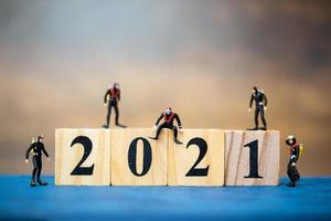 Miniature divers diving around wooden blocks with the number 2021, Happy New Year concept photo