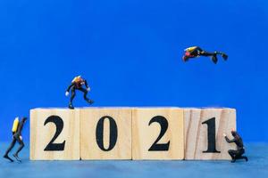 Miniature divers diving around wooden blocks with the number 2021, Happy New Year concept photo