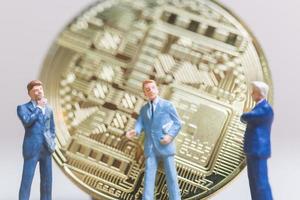 Miniature businessmen standing in front of a Bitcoin cryptocurrency coin, business concept photo