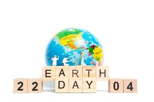 Miniature painters painting on a globe with wooden blocks showing Earth Day 22 04 on a white background, Earth Day concept photo