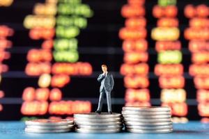 Miniature businessman standing on stacks of coins with a graph display in the background photo