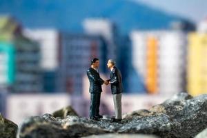 Miniature businessmen standing on a rock with buildings in the background photo