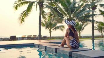 Mujer asiática sentarse alrededor de la piscina mirando al atardecer video