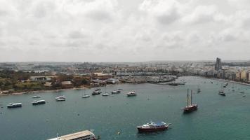 Aerial 4k drone footage panning from a harbor with anchored sea vessels and revealing a cityscape of the Mediterranean island town of Sliema, Malta.