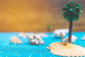 Miniature people wearing swimsuits relaxing on a seashell with a glitter background photo