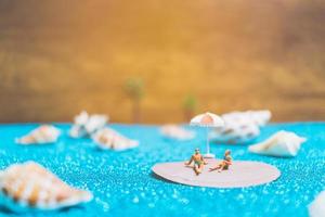 Miniature people wearing swimsuits relaxing on a seashell with a glitter background photo