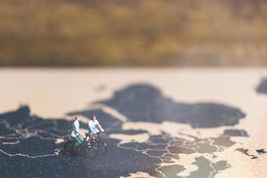 Miniature travelers riding bicycles on a world map, traveling and exploring the world concept photo