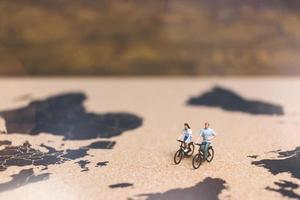 Miniature travelers riding bicycles on a world map, traveling and exploring the world concept photo