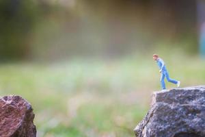 Miniature people running on a rock cliff with nature background, health and lifestyle concept photo