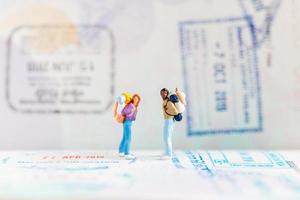 Viajeros en miniatura con mochilas caminando sobre un pasaporte, concepto de viaje y aventura.