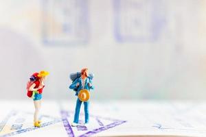 Miniature travelers with backpacks walking on a passport, travel and adventure concept photo