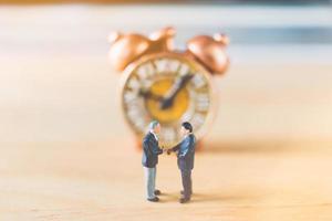 Miniature businessmen standing with an old clock on a wooden background photo