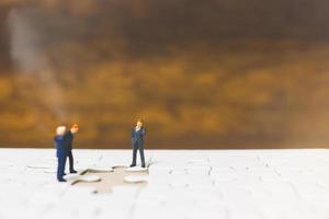 Miniature businessmen standing on jigsaws with a wooden background, business concept photo