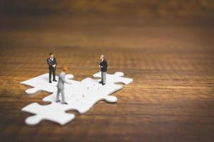 Miniature businessmen standing on jigsaws with a wooden background, business concept photo