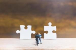 Miniature businessmen standing on jigsaws with a wooden background, business concept photo