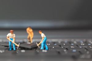 Equipo de ingenieros en miniatura que reparan una computadora portátil con teclado, concepto de reparación de computadoras foto