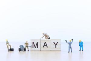 Miniature people working on wooden blocks with the word May on a wooden floor photo