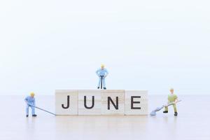 Miniature people working on wooden blocks with the word June on a wooden floor photo