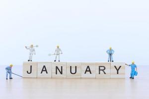 Miniature people working on wooden blocks with the word January on a wooden floor photo