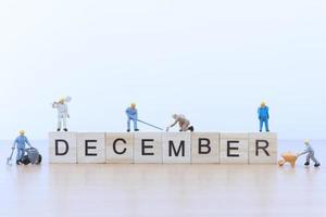 Miniature people working on wooden blocks with the word December on a wooden floor