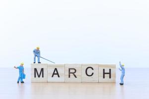 Miniature people working on wooden blocks with the word March on a wooden floor photo