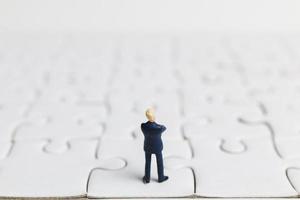 Miniature businessman standing on a white jigsaw puzzle, business concept photo