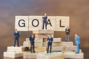 Miniature businessmen standing on wooden blocks with the word Goal, business career growth concept photo