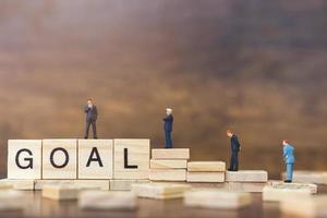 Miniature businessmen standing on wooden blocks with the word Goal, business career growth concept photo