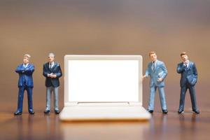 Miniature businesspeople thinking with a project for presenting investments on a white screen computer laptop, business and technology concept photo