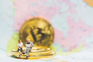 Miniature businesspeople on a stack of cryptocurrency coins with a world map in the background, money and financial business success concept photo