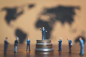 Miniature businessmen on a stack of coins with a world map in the background, money and financial business success concept photo