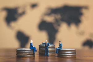 Miniature businessmen on a stack of coins with a world map in the background, money and financial business success concept photo