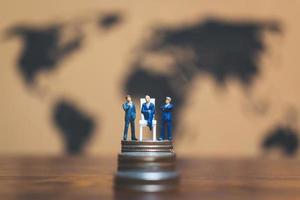 Miniature businessmen on a stack of coins with a world map in the background, money and financial business success concept photo