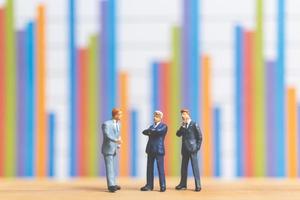 Miniature businessmen standing in front of a business graph background, business growth concept photo