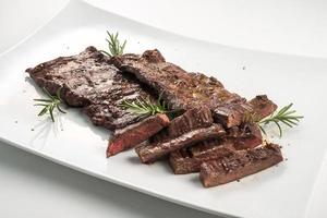 Square white plate of sliced skirt steak and rosemary photo