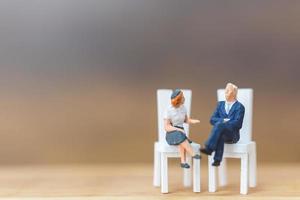 Miniature people sitting on chairs on a wooden background photo