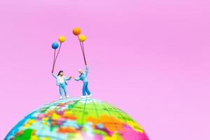 Miniature family holding balloons on a globe with a pink background