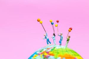 Miniature family holding balloons on a globe with a pink background photo