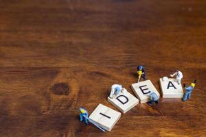 Miniature people standing with wooden blocks with the word Idea on a wooden background photo