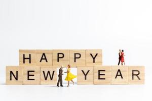 Miniature people dancing on wooden blocks with the text Happy New Year on a white background
