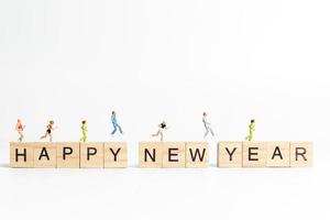 Miniature people running on wooden blocks with the text Happy New Year on a white background photo