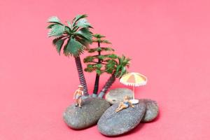 Miniature people wearing swimsuits relaxing on a rock with a pink background photo