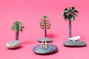 Miniature people wearing swimsuits relaxing on a rock with a pink background photo