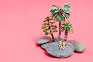 Miniature people wearing swimsuits relaxing on a rock with a pink background photo